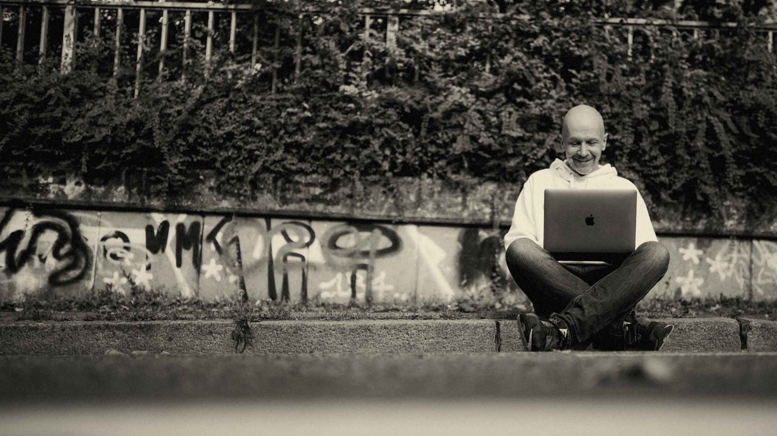 Webdesigner Paul Jackson sitzt am Bordstein mit Laptop „am Arbeiten“