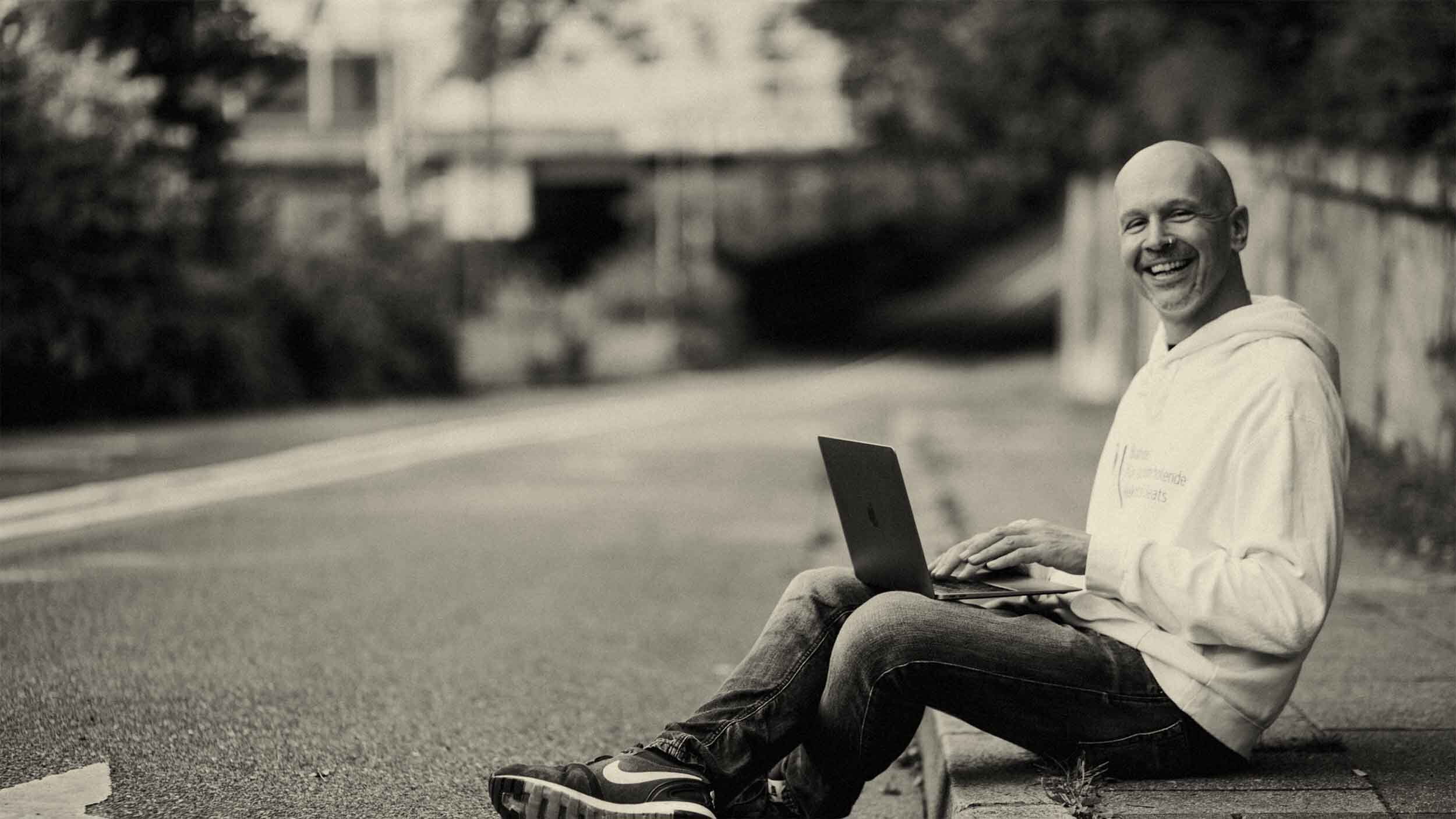 Web designer Paul Jackson sits on the kerb with his laptop and smiles
